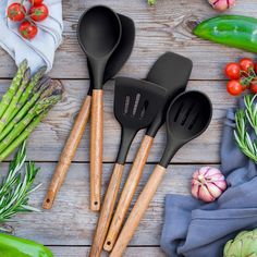 four kitchen utensils on a wooden table with vegetables and herbs in the background