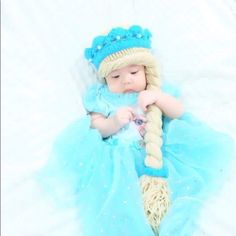 a baby wearing a blue and white dress laying on top of a snow covered ground