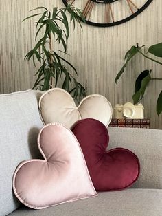 three heart shaped cushions on a couch in front of a clock and plant behind it