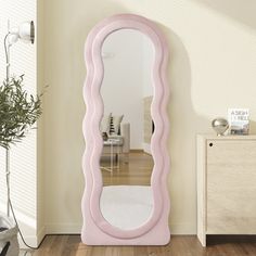 a large pink mirror sitting on top of a wooden floor next to a white dresser