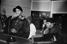 a black and white photo of some people in a recording studio, one with a microphone