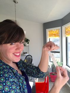 a woman standing in front of a window holding something up to her face and smiling at the camera