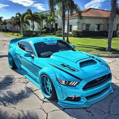 a blue mustang parked on the side of a road next to palm trees and buildings