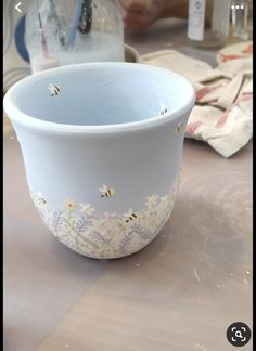 a white bowl with flowers and bees painted on the side sitting on a counter top