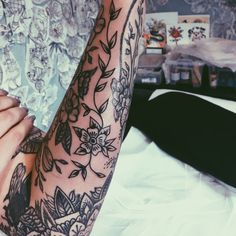 a woman's arm with tattoos on it sitting on top of a white bed