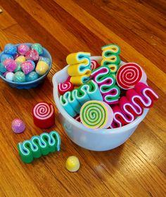 a bowl filled with candy next to colorful candies on top of a wooden table