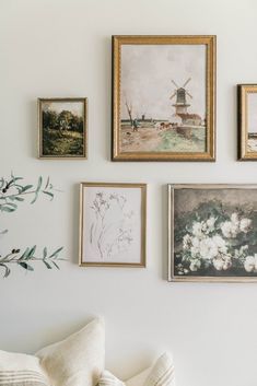 several framed pictures hang on the wall next to a white couch with pillows and throw pillows