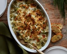 a casserole dish with cheese and artichokes on the side next to slices of bread