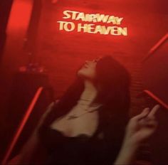 a woman standing in front of a red neon sign that says stairway to heaven on it