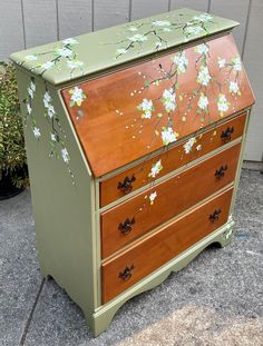 an old dresser with flowers painted on the top and bottom drawers is sitting in front of a house