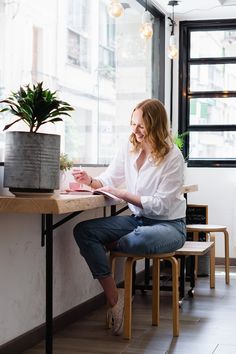 a woman sitting at a table in front of a potted plant and reading a book