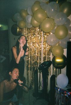 two women singing into microphones in front of balloons and streamers on the wall