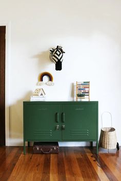 a green cabinet sitting on top of a hard wood floor next to a white wall