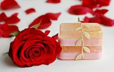 a rose sitting next to a soap bar with leaves on it and petals scattered around