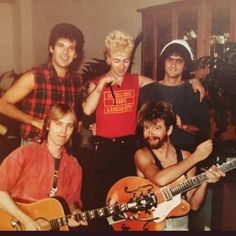 a group of young men standing next to each other holding guitars and posing for the camera