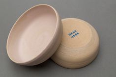 two white bowls sitting next to each other on top of a gray surface with blue writing