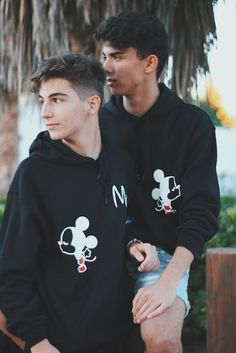 two young men standing next to each other wearing mickey mouse sweatshirts on their hoodies