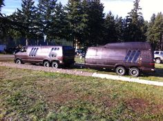 two brown vans parked next to each other on the side of a road with trees in the background