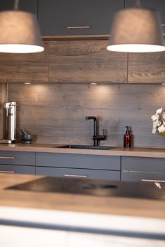 a kitchen with two lights hanging over the sink and counter top, in front of a wooden paneled wall