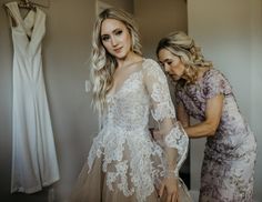 two women standing next to each other in front of wedding gowns and dresses hanging on the wall