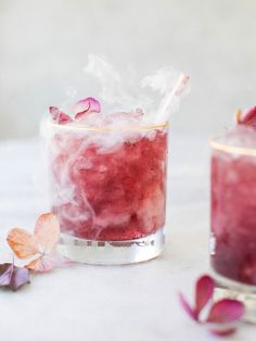 two glasses filled with drinks sitting on top of a white table next to pink flowers