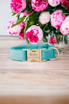 a blue dog collar with a name plate and flowers in front of it on a wooden table