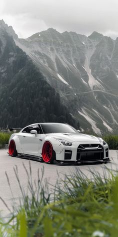 a white car with red rims parked in front of mountains