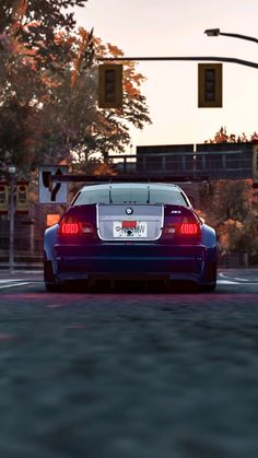 a blue sports car driving down a street next to a traffic light and some trees