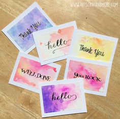 four watercolor cards with the words hello written in black ink on them, sitting on top of a wooden table