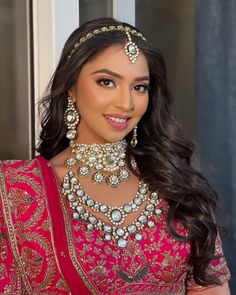 a woman wearing a red and gold bridal outfit with jewelry on her neck, standing in front of a window