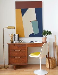 a desk with a yellow chair and a painting on the wall above it in an office