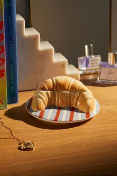 a croissant sitting on a plate next to a book and perfume bottle in the background