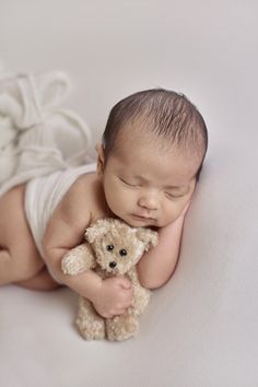 a newborn baby is holding a teddy bear