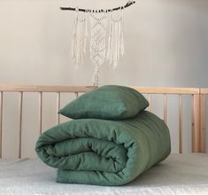 two green pillows stacked on top of each other in front of a crib with a dream catcher hanging above it