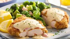 two pieces of chicken on a plate with lemon sauce and broccoli, next to a side of salad