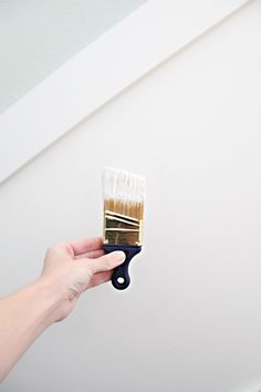 a person holding a paint brush in their left hand and painting the wall with white paint