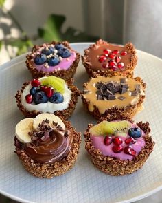 four cupcakes on a white plate topped with fruit and nutty toppings