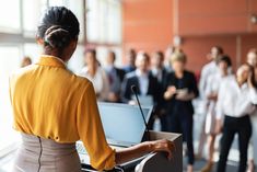 a woman standing in front of a laptop computer next to a crowd of other people