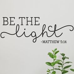 a wall decal with the words be the light and a potted plant next to it