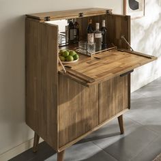 a wooden cabinet with two bottles on it and some green apples in the bottom drawer