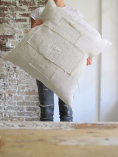 a woman holding a pillow in front of a brick wall