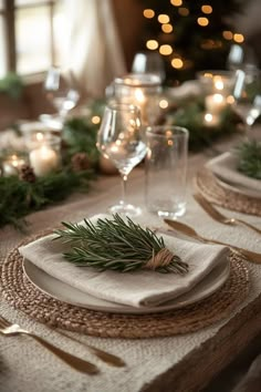 a table set for christmas dinner with candles and greenery on the placemats