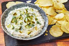 a bowl of potato chips and dip on a black tray next to some crackers