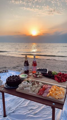 a table that has food on it near the ocean at sunset or sunrise with water and clouds in the background