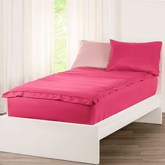 a white bed with pink sheets and pillows