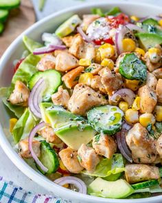 a white bowl filled with chicken, cucumber and tomato salad next to a wooden spoon