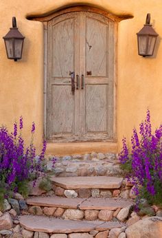 an old door and some purple flowers in front of a stone steps leading up to it