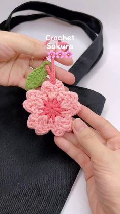 a person is holding a crochet flower in their left hand and the other hand has a black tote bag on it