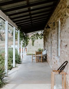 a porch with chairs and plants on the side of it next to a stone building