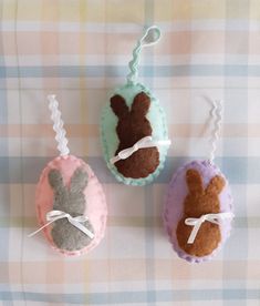 three felt easter bunnies with bunny ears tied to them on a checkered table cloth